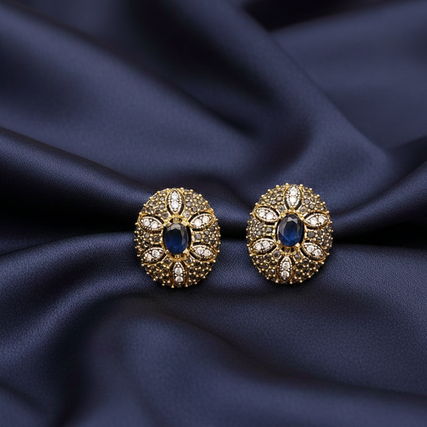 Pair of gold and blue earrings on a dark blue fabric background