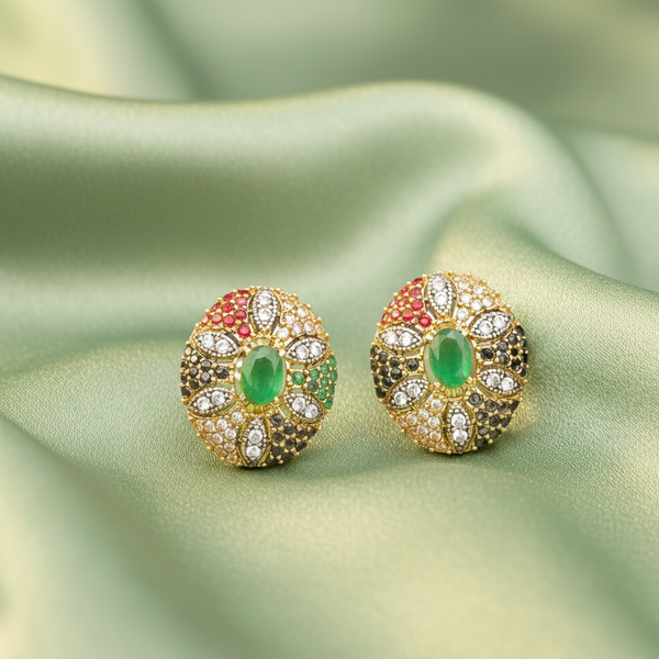 Pair of gold earrings with green and red gemstones on a light green fabric background