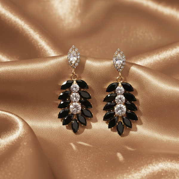 Pair of black and clear gemstone earrings on a gold satin background