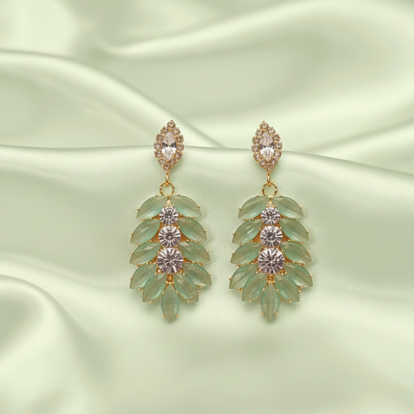 Pair of green leaf-shaped earrings with gold and silver accents on a light green satin background.